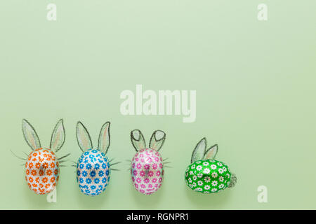 Four chocolate eggs in colorful aluminium foil with painted easter bunny ears on green background Stock Photo