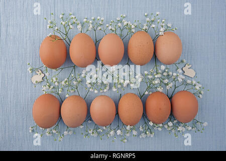 Eggs ecru in two rows between Gypsophila and Easter bunnies on woven tablecloth Stock Photo