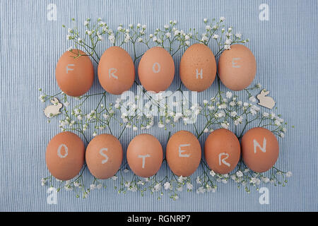 Eggs ecru in two rows between Gypsophila and Easter bunnies on woven tablecloth Stock Photo