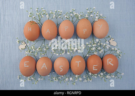 Eggs ecru in two rows between Gypsophila and Easter bunnies on woven tablecloth Stock Photo