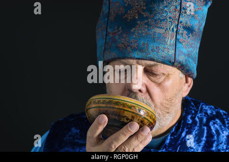 Nice portrait of bearded senior man in blue oriental clothes drinking tea from piola Stock Photo
