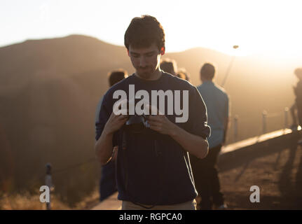 Young guy looking at camera?in hands near people on mountain at sunset in San Francisco, USA Stock Photo