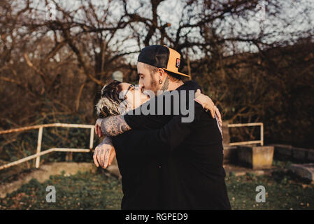 Side view of bearded man embracing and kissing young lady in eyeglasses in park on blurred background Stock Photo