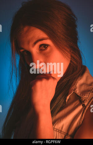 Charming young lady with piercing and fist near mouth looking at camera in redness on blue background Stock Photo