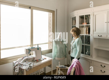 Senior female adjusting beautiful ornamental garment on dummy while working in cozy workshop Stock Photo
