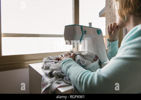 Friendly mature female sewing on modern machine in cozy workshop Stock Photo