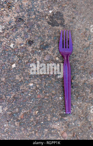 A Close up view of a purple plastic fork lying on the tar on a outside parking lot Stock Photo