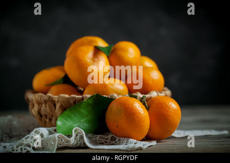 Tangerines with leaves in basket on rustic wooden background. Stock Photo