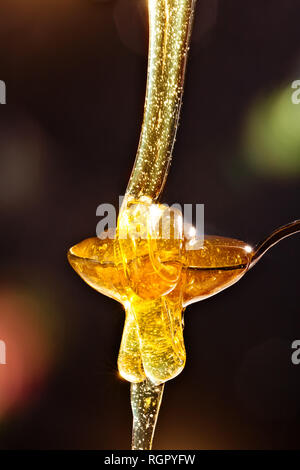 Honey with gold color flows down from a spoon, on a dark background. Healthy eating. Diet. Selective focus. Stock Photo