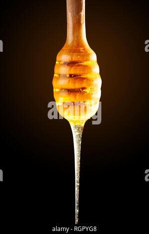 Honey with gold color flows down from a spoon, on a dark background. Healthy eating. Diet. Selective focus. Stock Photo