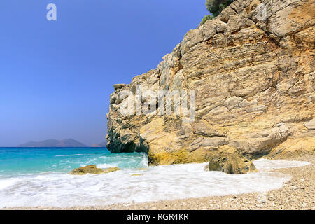 large foam in front of the waves, left sea, right beach, big mountain in the center, splashing waves Stock Photo
