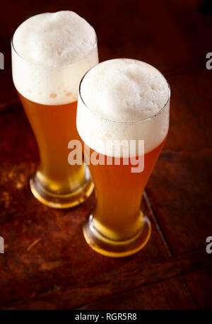 Two tall elegant pint glasses of cold wheat beer with a frothy head on a  wooden bar table conceptual of Oktoberfest Stock Photo - Alamy