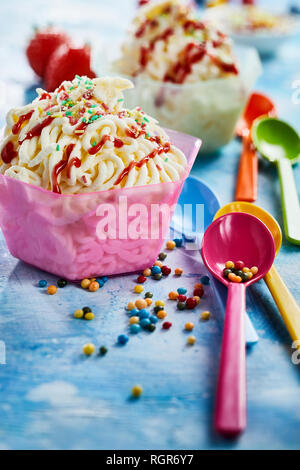Cups of spaghetti ice cream raspberry dessert with plastic spoons against blue background Stock Photo