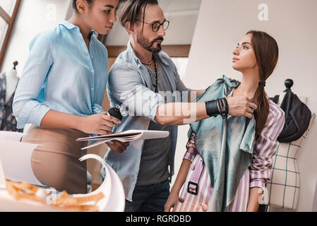 Taking measures and chooseing material. Group of three people at design studio. Man measuring material to a woman Stock Photo