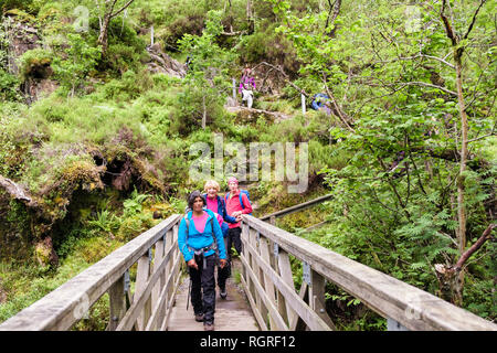 Senior hikers crossing footbridge across River Coe from Lost Valley or Coire Gabhail. Glen Coe Pass, Glencoe, Lochaber, Highland, Scotland, UK Stock Photo