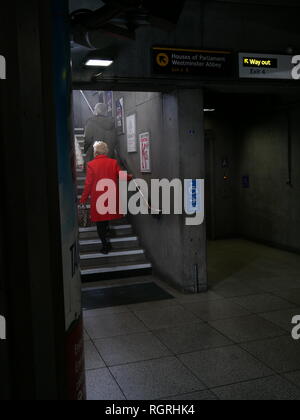 A lady in a red coat ascends the stairs at Westminster underground station in London. Stock Photo