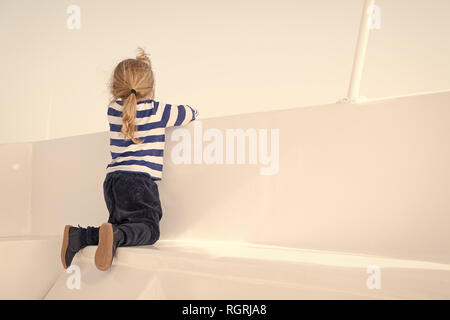 Small boy look from ship board, back view. Child on seat of boat on sunny blue sky. Kid with blond hair in navy clothes. Kids fashion and style. Summer vacation, travelling and wanderlust concept. Stock Photo