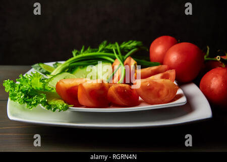 sliced tomatoes cucumbers lying on a white plate decorated with green onions standing on a dark wooden table Stock Photo