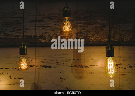 Three decorating light bulbs of warm color on dark wood background. Stock Photo