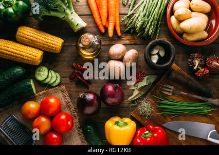 Assorted fresh vegetables and bottle of oil lying on timber tabletop near various cooking tools Stock Photo