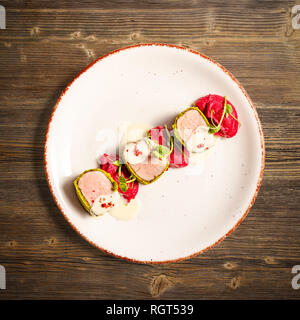 Flat lay of green crusted pork loin, mashed potatoes with beetroot and cheese sauce on wooden background Stock Photo