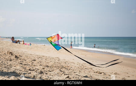 A rainbow colored kite flying low over the beach with families and vacationers in the background. Stock Photo