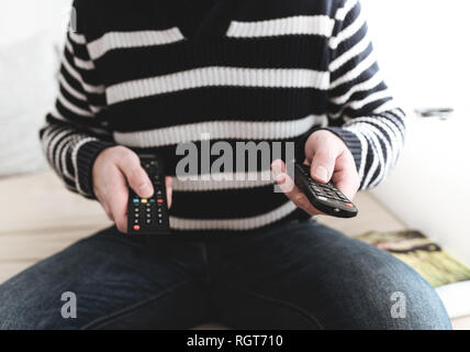 man sitting on sofa holding remote control in each hand Stock Photo