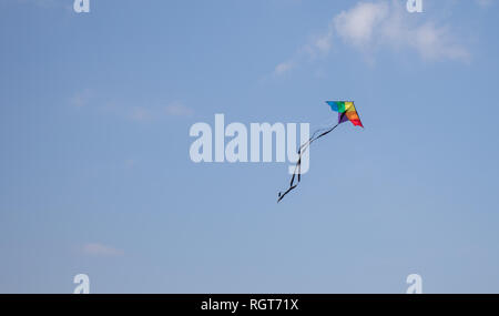 A rainbow colored kite soaring high in the blue sky on a bright and sunny day. Stock Photo