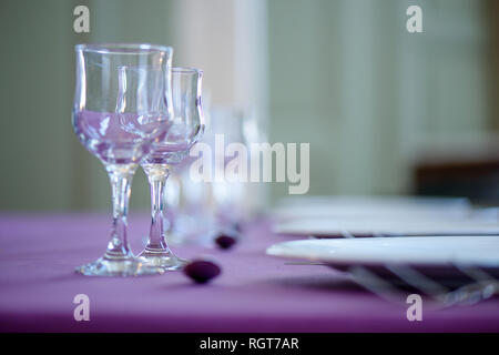 Clean table setting for fine dining with striking, elegant purple table cloth and focus on two crystal glasses for water and wine and white china Stock Photo
