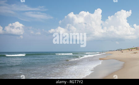 A photo of the shoreline with a pier far off in the distance and vacationers along the beach.  Waves crashing ashore. Stock Photo