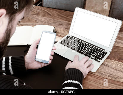 man using laptop while looking at his smart phone Stock Photo