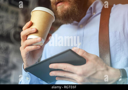Businessman using digital tablet and drinking coffee. Smartphone Paper Cup Shirt Beard. Office Coffee Break Concept Stock Photo