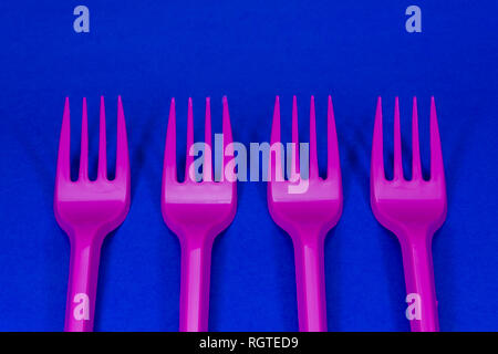 Pink cutlery plastic forks arranged on blue background. Plastic waste problem concept Stock Photo