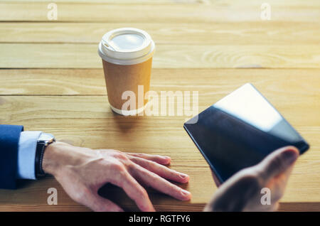 Businessman at a table in a cafe. Cup of coffee Tablet Blazer Hands Wooden table. Coffee Break Concept Stock Photo