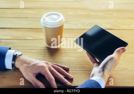 Businessman at a table in a cafe. Cup of coffee Tablet Blazer Hands Wooden table. Coffee Break Concept Stock Photo