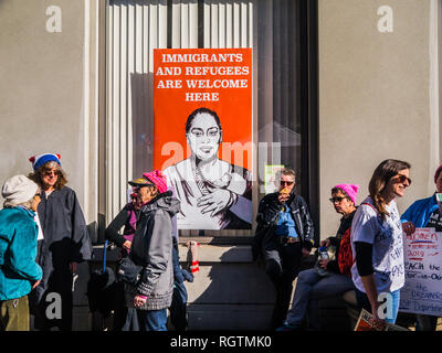 OAKLAND, CA/USA - January 20, 2018: Sign reads 'Immigrants and refugees are welcome here' while unidentified participants walk by at the Women's March Stock Photo