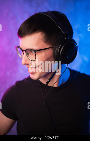 Gamer or streamer in earphones with microphone over colorful pink and blue neon lit wall Stock Photo