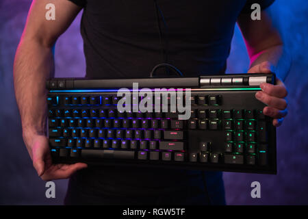 Close-up on gamer's hands holding a keyboard. Background is lit with neon lights Stock Photo