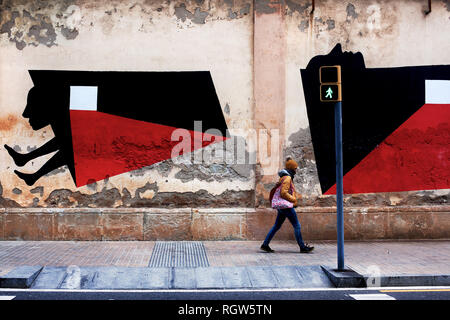 Woman walking past murals on Barcelona's old prison walls, Barcelona, Spain. Stock Photo