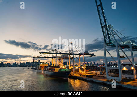 Miami, USA - March 01, 2016: cargo ship and cranes in sea port on evening sky. Maritime container port or terminal. Shipping freight and merchandise. Water transport and transportation concept  Stock Photo