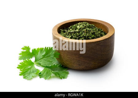 Dried chopped coriander leaves in a dark wood bowl next to fresh coriander leaves isolated on white. Stock Photo