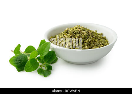 Dried chopped oregano in white ceramic bowl next to fresh oregano leaves isolated on white. Stock Photo