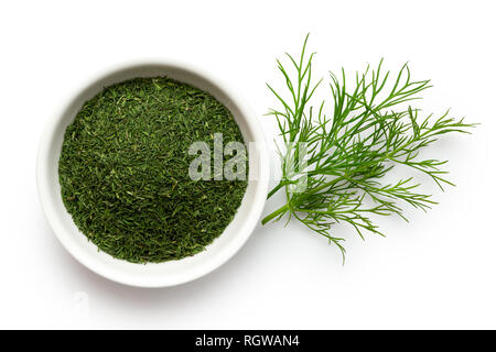Dried chopped dill in white ceramic bowl next to fresh dill leaves isolated on white from above. Stock Photo