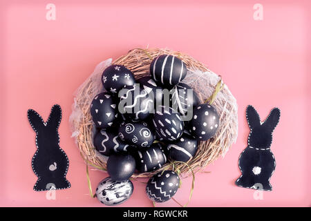 Easter composition from eggs of the black colors with creative light pattern, handmade in a round nest made of hay ,and the Easter Bunny in black colo Stock Photo