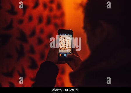 Back view of crop human taking photo on mobile phone of wall with painted birds in redness on blurred background in Chefchaouen, Morocco Stock Photo