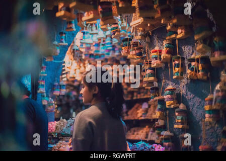 Side view of young Woman in shop with hanging colorful decorations in Chefchaouen, Morocco Stock Photo
