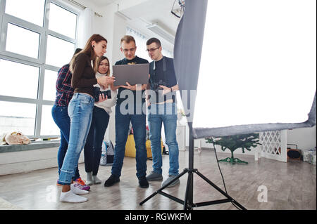 Photographer explaining about the shot to his team in the studio and looking on laptop. Talking to his assistants holding a camera during a photo shoo Stock Photo