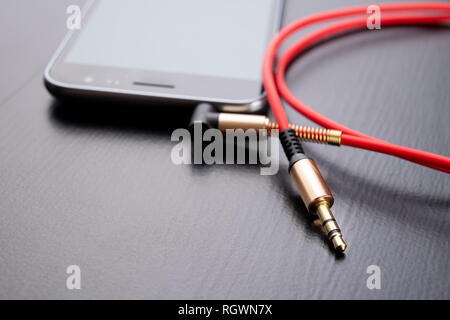Jack cable for connecting headphones. Telephone and accessories on the table. Dark background. Stock Photo