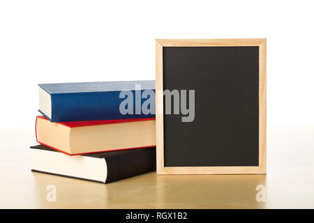 Empty, blank, black chalkboard with stack of books on brown wooden desk over white background Stock Photo