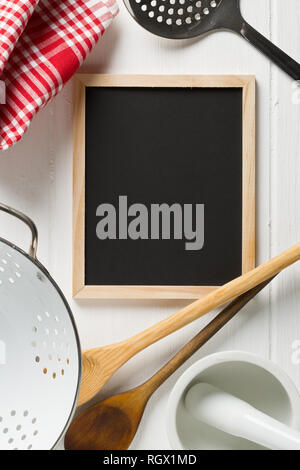 Blank, empty, black chalkboard with cooking utensils and red checkered dish towel flat lay from above on white wooden table with copy space Stock Photo
